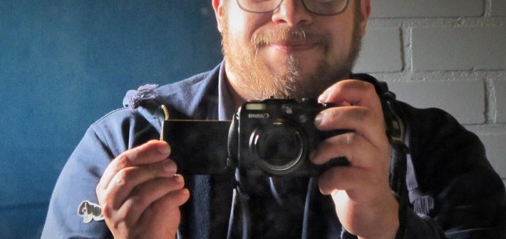 Kuvassa on mies valokuvakameran kanssa. Hän on Oscar Ortiz-Nieminen on taidehistorioitsija, joka on vetänyt queer-opastuksia museoissa vuodesta 2015.