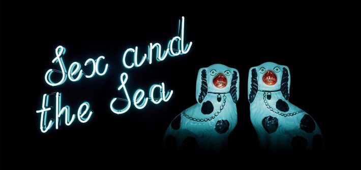 Kuvassa on kaksi hohtavaa koirapatsasta sekä hohtava teksti Sex and the Sea.