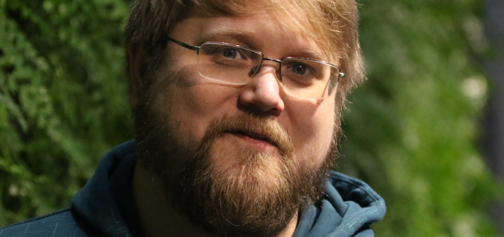 Hymyilevällä ja parrakkaalla Pekka Rantalalla on silmälasit ja huppari. Hänen takanaan on viherseinä.