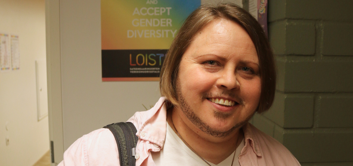 Hymyilevä Late Mäntylä Setan toimistolla. Hänellä on polkkatukka ja parta, vaaleanpunainen kauluspaita ja ristiriipus kaulassa. Toisella olalla roikkuu reppu.