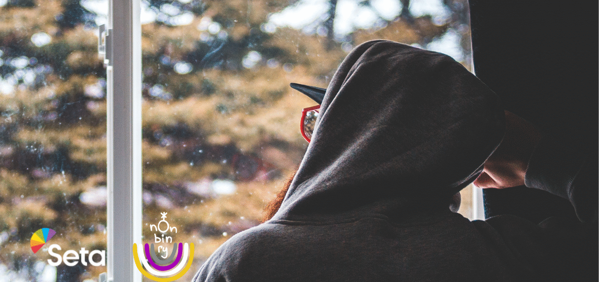 Huppariin pukeutunut henkilö selin ikkunan edessä. Ikkunasta näkyy talvinen maisena.