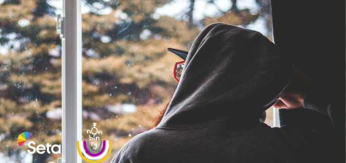 Huppariin pukeutunut henkilö selin ikkunan edessä. Ikkunasta näkyy talvinen maisena.